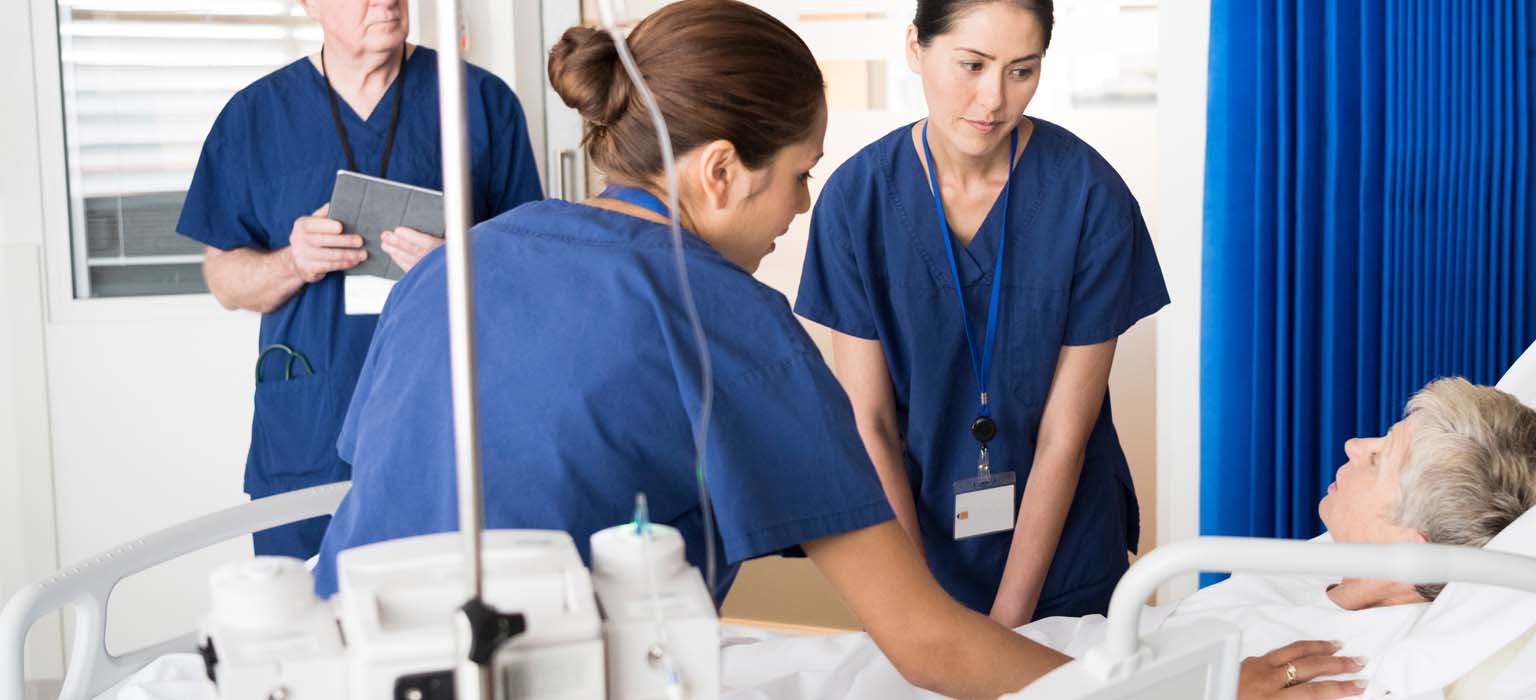 Nurses assisting an elderly woman in a hospital bed.